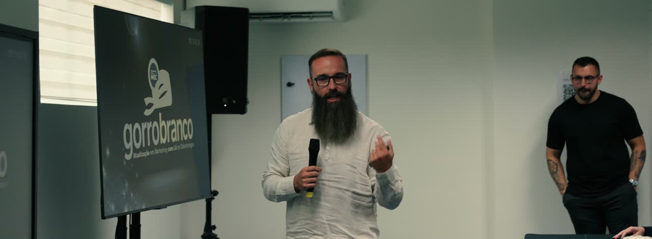 Matheus Marcondes falando de microfone na sala de aula, com o slide do Novo Gorro Branco atrás