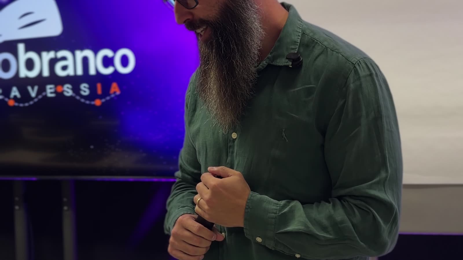 Matheus Marcondes falando de microfone na sala da imersão, com o telão do Novo Gorro Branco atrás